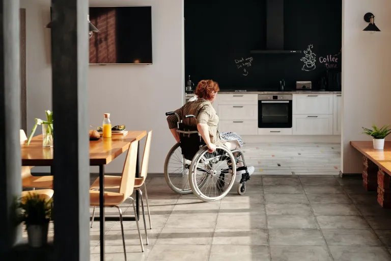 Eine an Parkinson erkrankte Seniorin fährt mit ihrem Rollstuhl durch ihre Wohnung